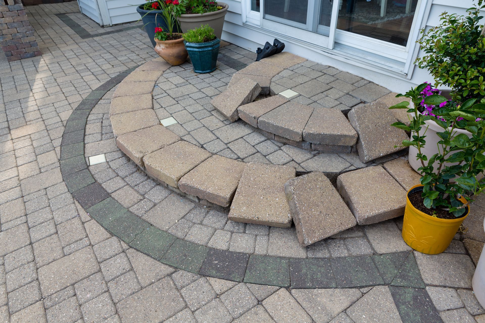 A semicircular patio step made of beige stone pavers, showing uneven placement and gaps in front of a sliding door.