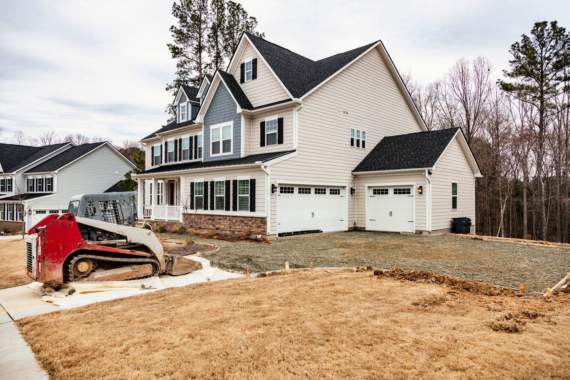 New house with white siding and garage, a red skid steer in front, and bare landscaping.