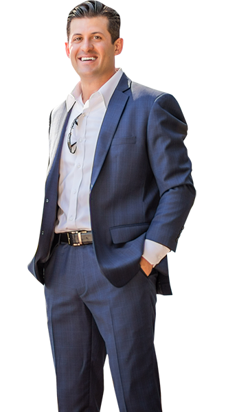 Joe in a suit and white shirt is standing with his hands in his pockets.