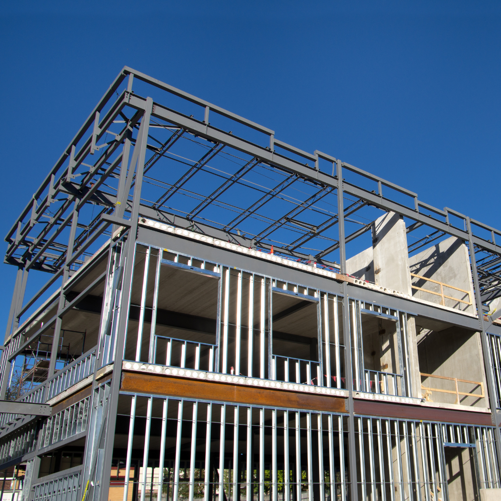 Steel frame of a multi-story building under construction against a clear blue sky.