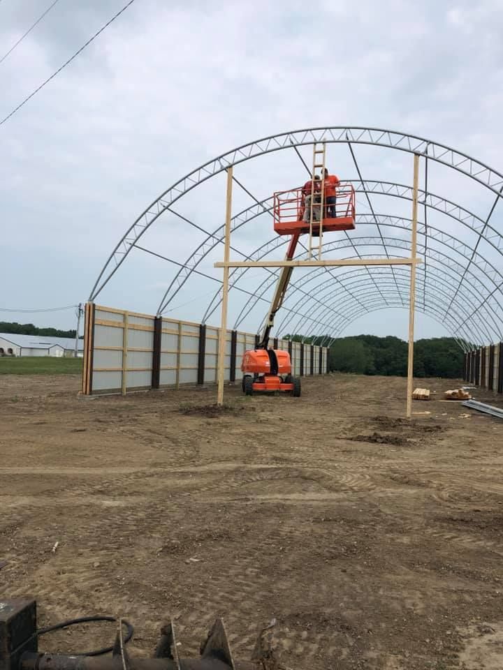 Construction worker in an orange lift building a greenhouse frame