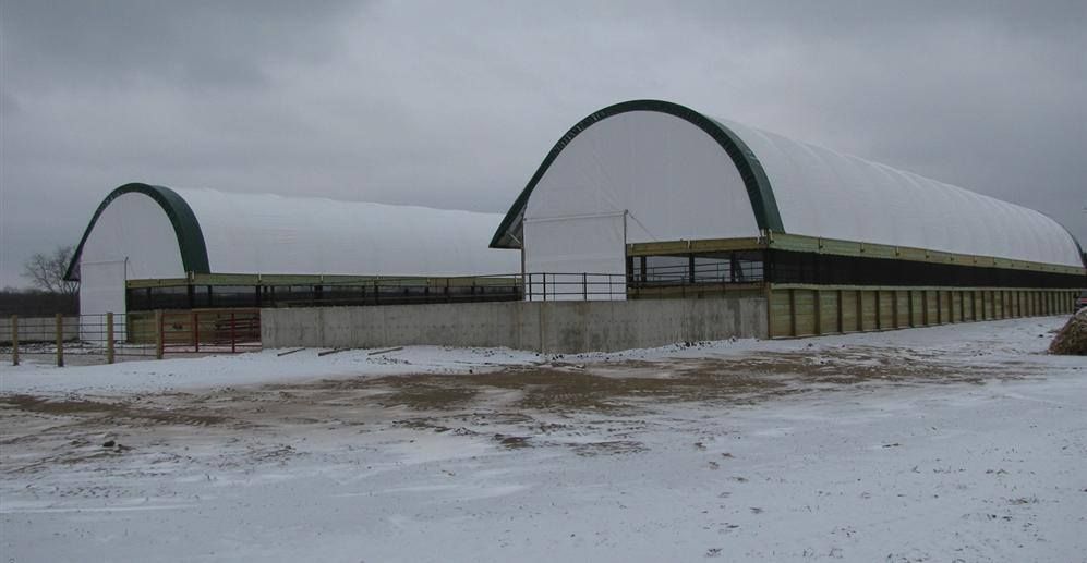 Two white arched roof buildings with dark green trim and snow-covered ground.
