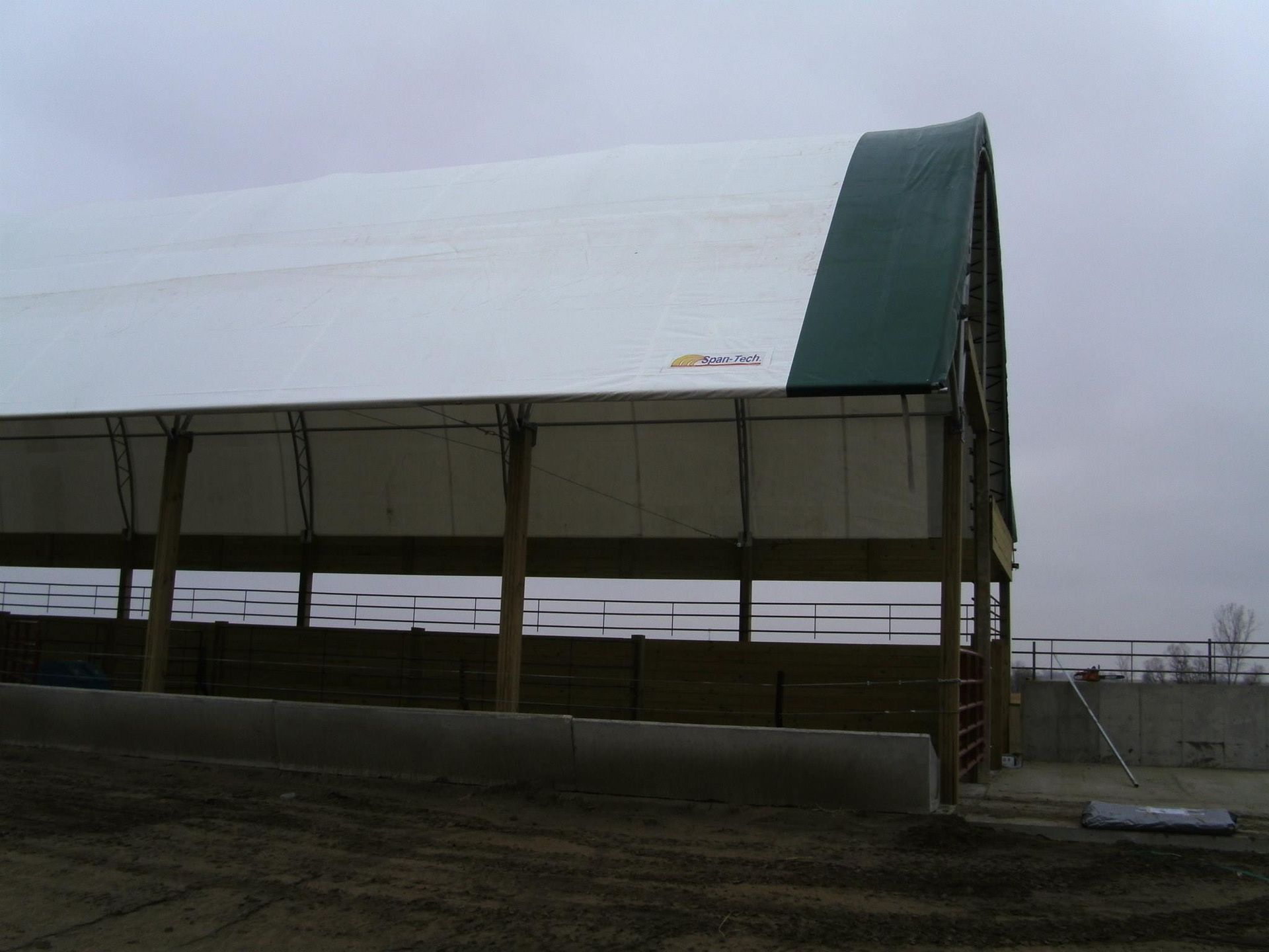 Barn with white roof, green arched end, open sides, and wooden supports on a cloudy day.