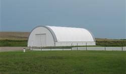 White arched-roof building on a grassy field, gray sky background.
