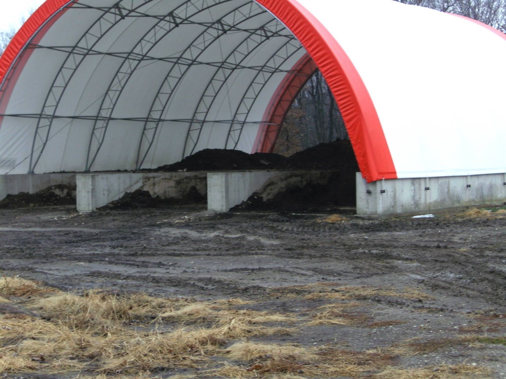 Compost storage structure with white cover and red arches, containing piles of dark compost.
