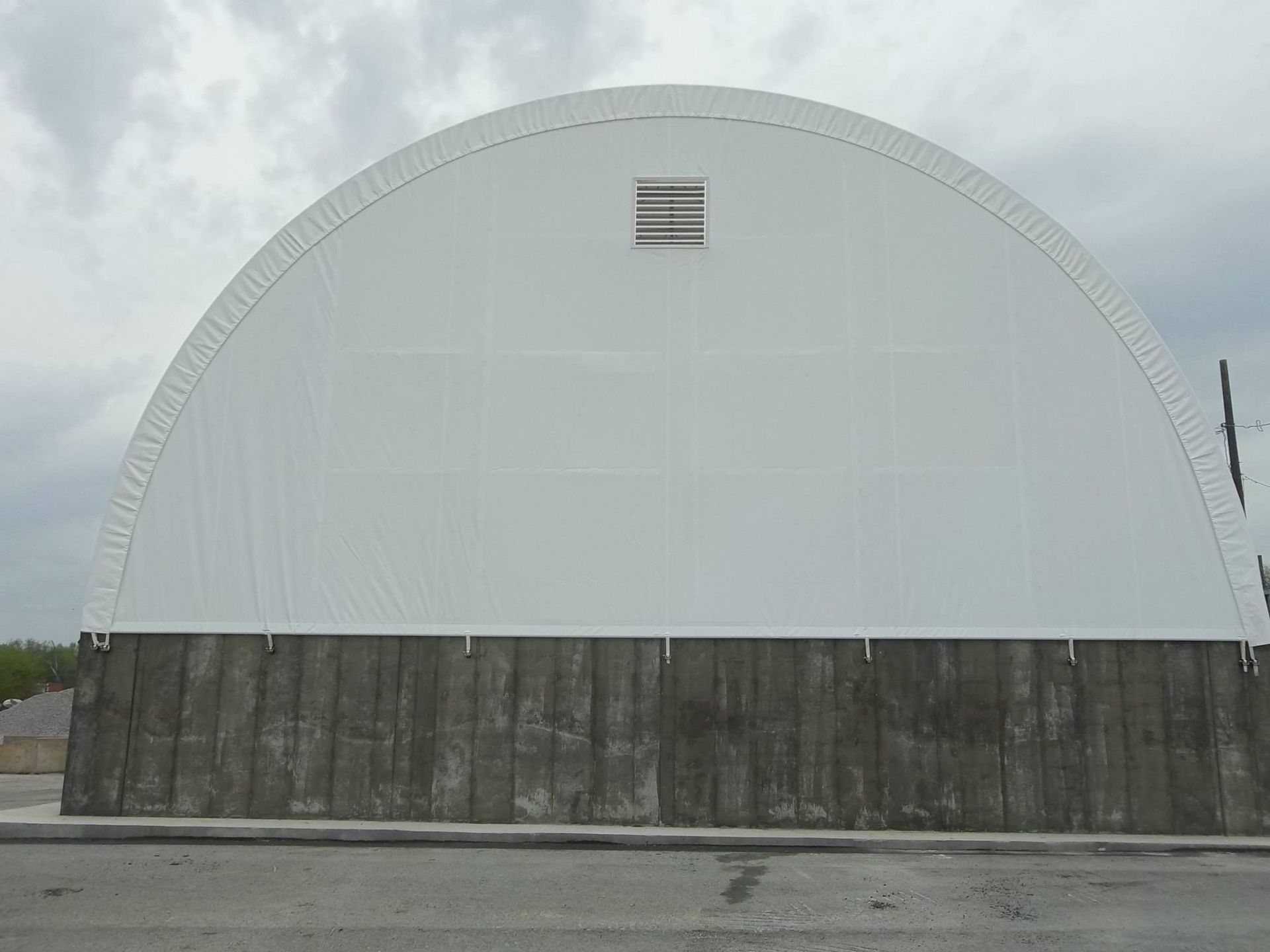 White arched building on a concrete base with a vent on the top. Overcast sky.