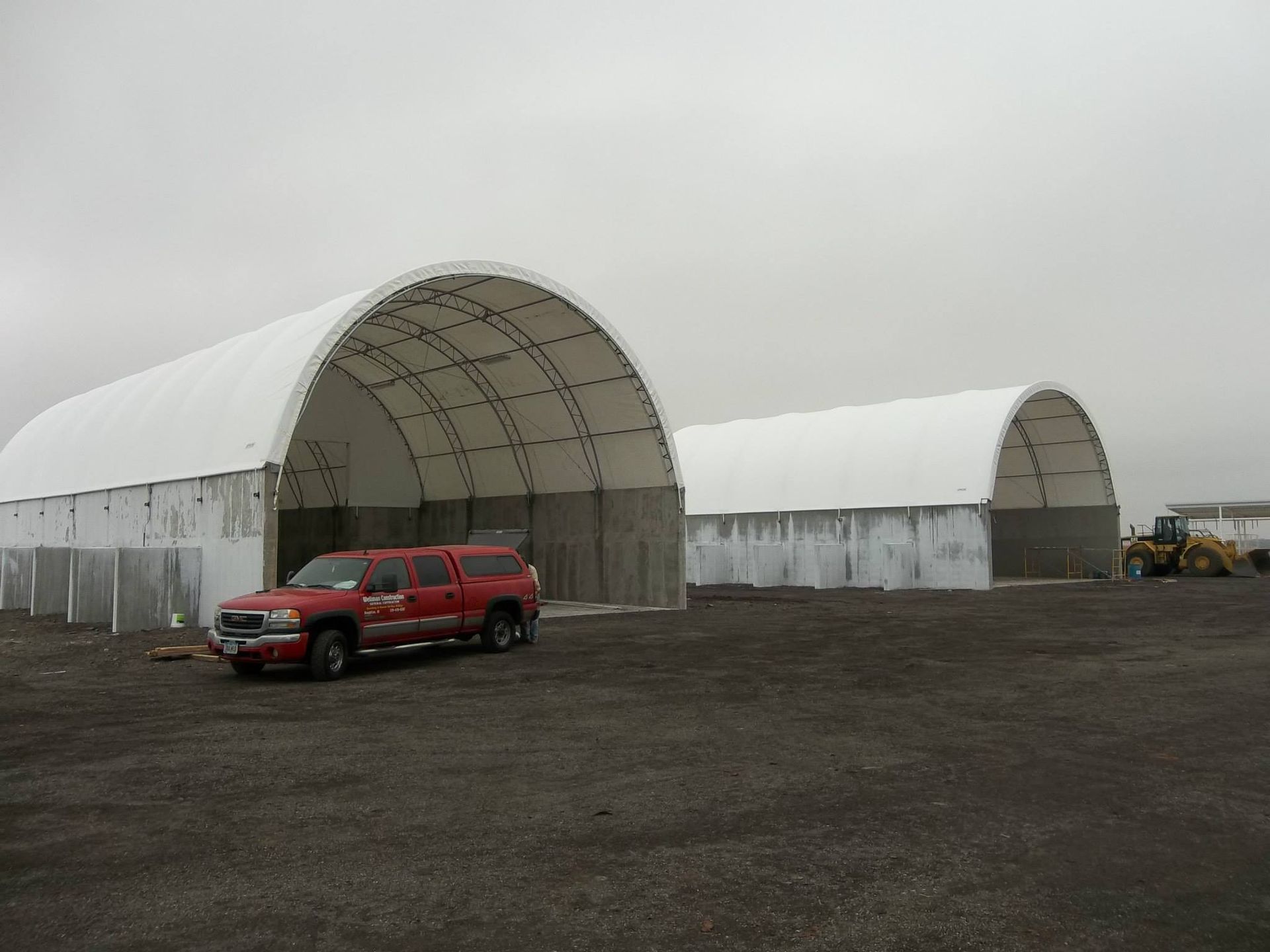 Two large white arched storage buildings, red truck, cloudy day.