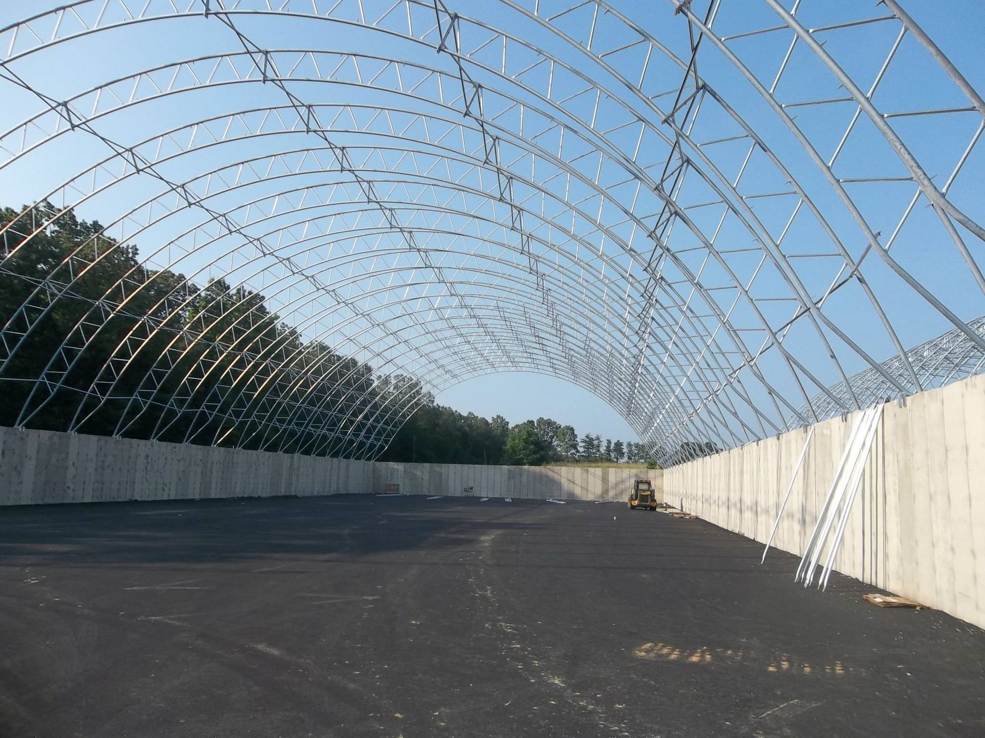 Metal frame structure over a dark surface, bordered by concrete walls and a tree line in the distance.