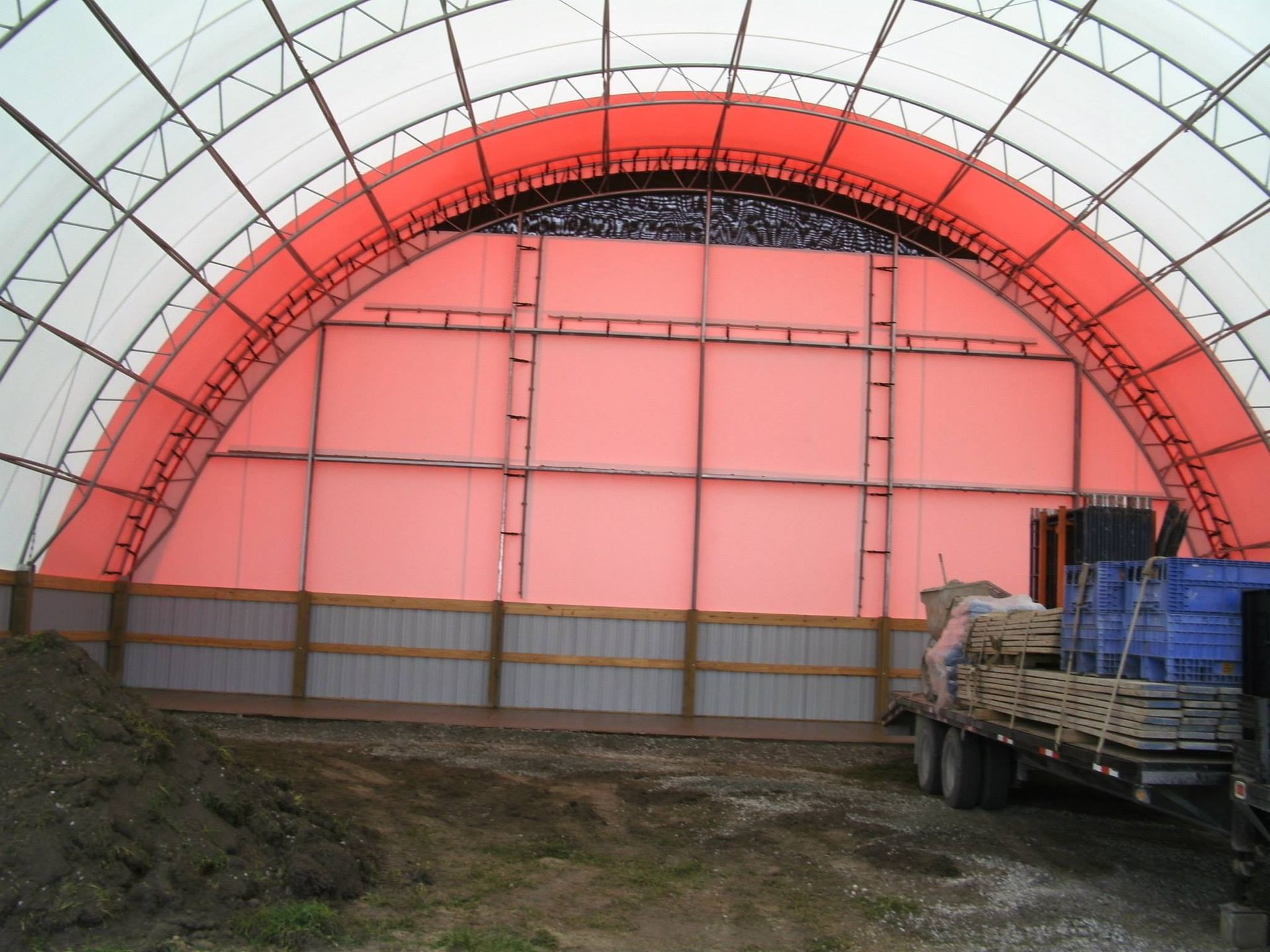 Interior of a large storage building. Red arched support, white fabric roof. Trailer parked inside.