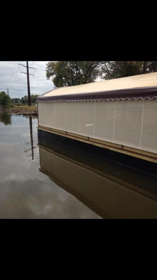 Houseboat on water reflecting the structure; brown roof and walls, overcast sky.