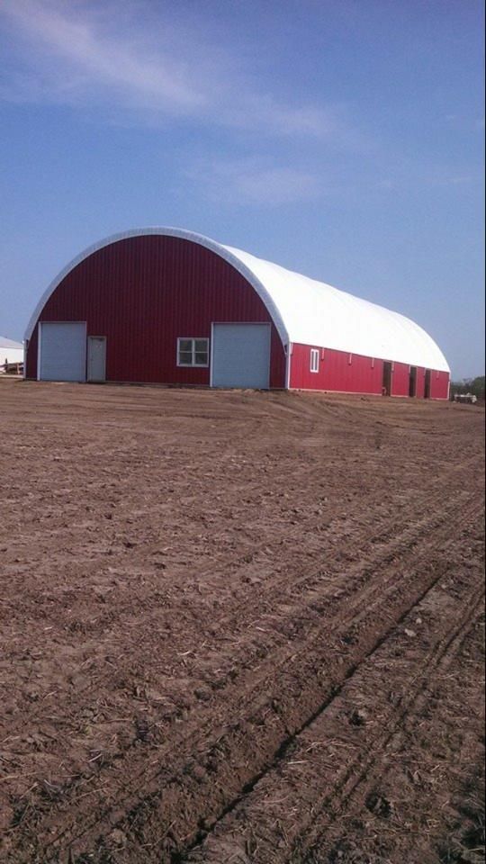 Red and white Quonset hut-style building on plowed field under a blue sky.