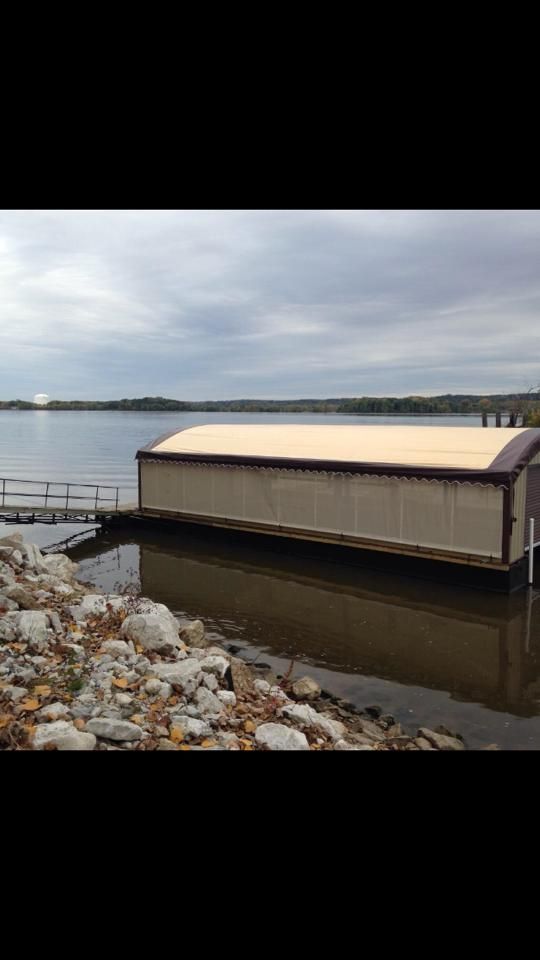 Boat house on a lake with a wooden dock and rocky shoreline under a cloudy sky.