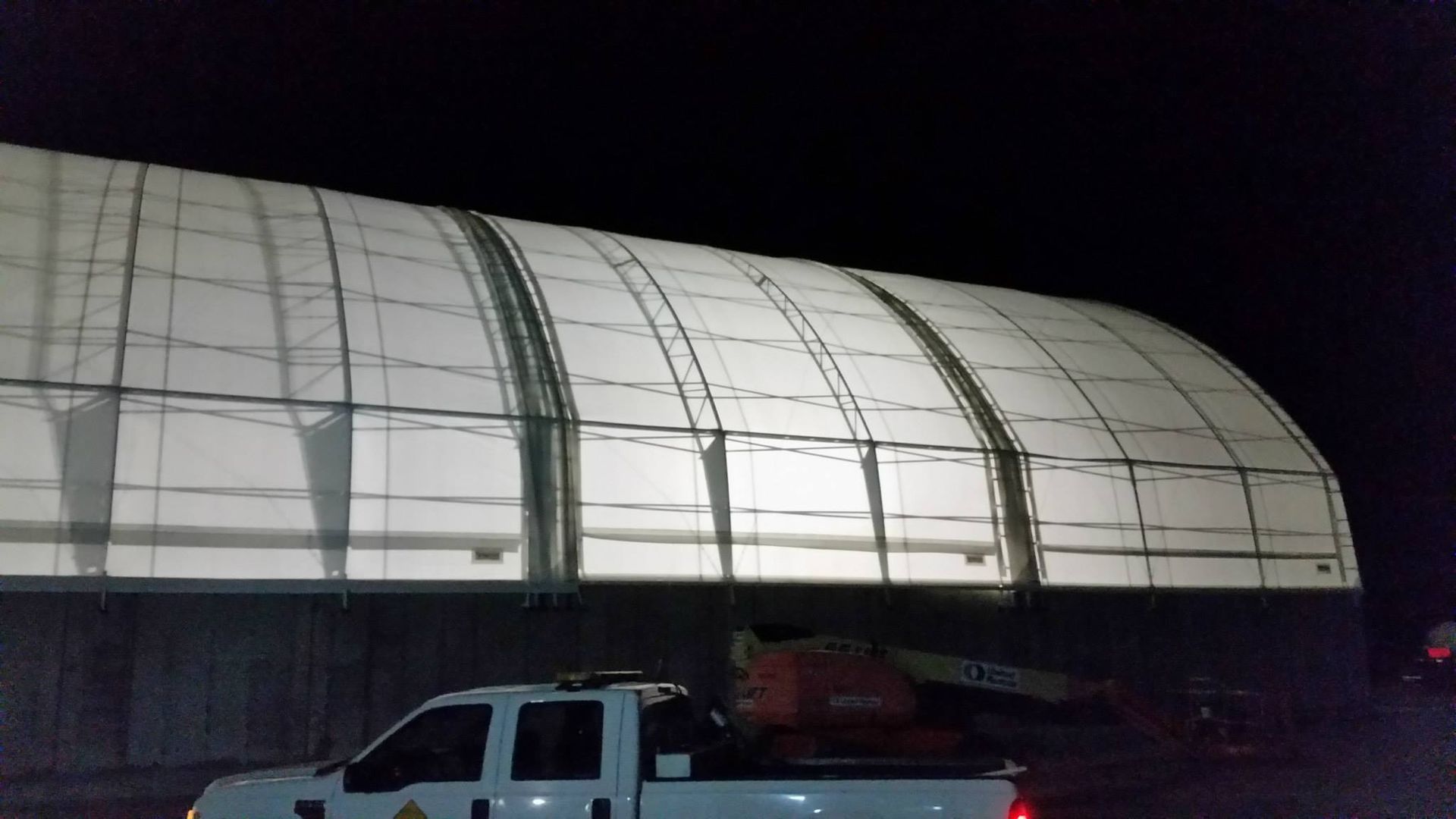 White arched building at night, lit from within, with a pickup truck in front.