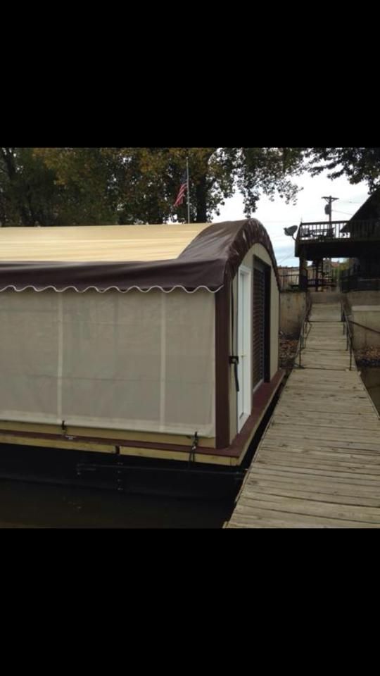 Houseboat with a brown roof and white siding, docked next to a wooden walkway.
