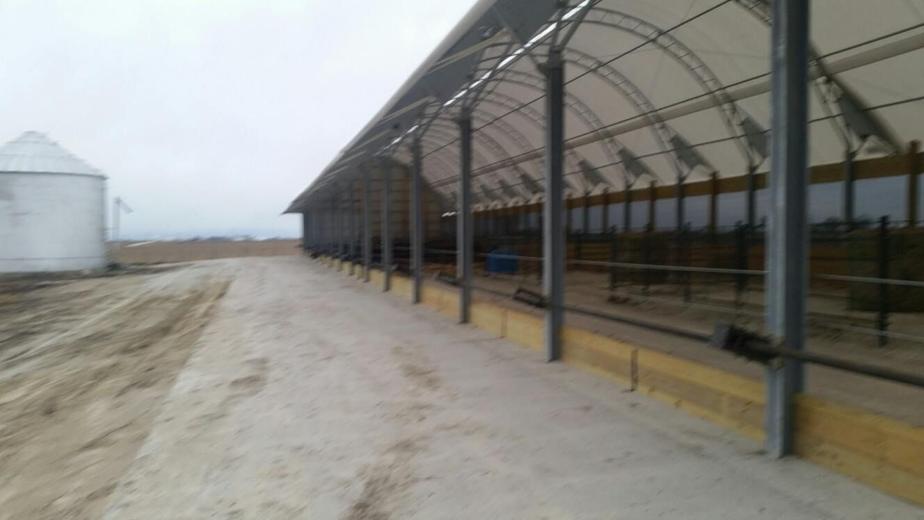 Long shed with a white roof, along a sandy path, and a silo in the background.