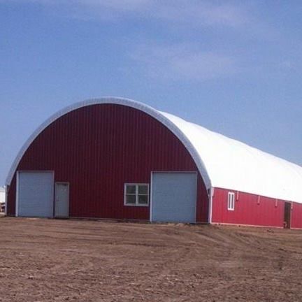 Red and white arched-roof building with two garage doors and a window, set on dirt under a blue sky.