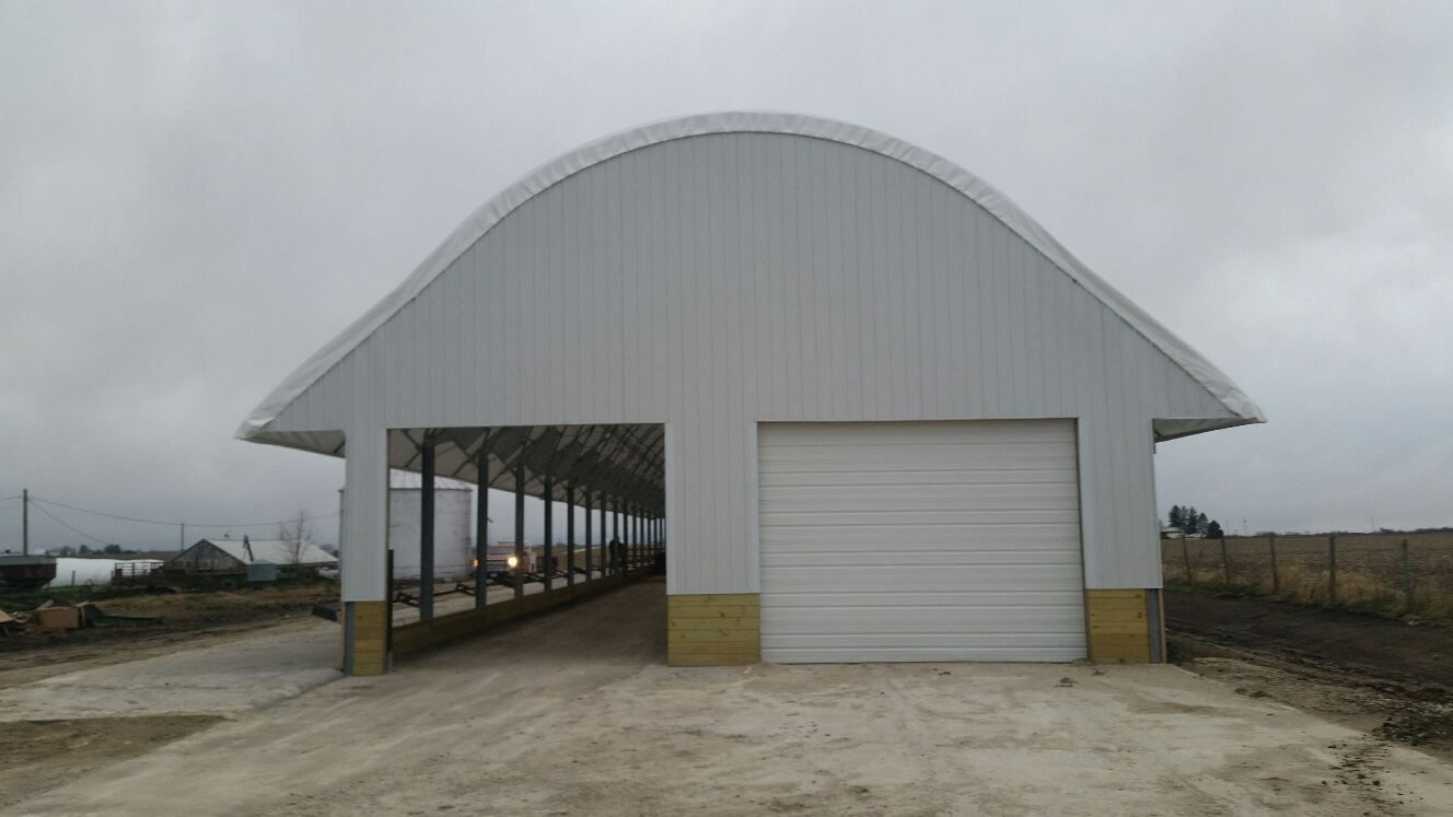White metal building with a curved roof and garage door. Cement floor and overcast sky.