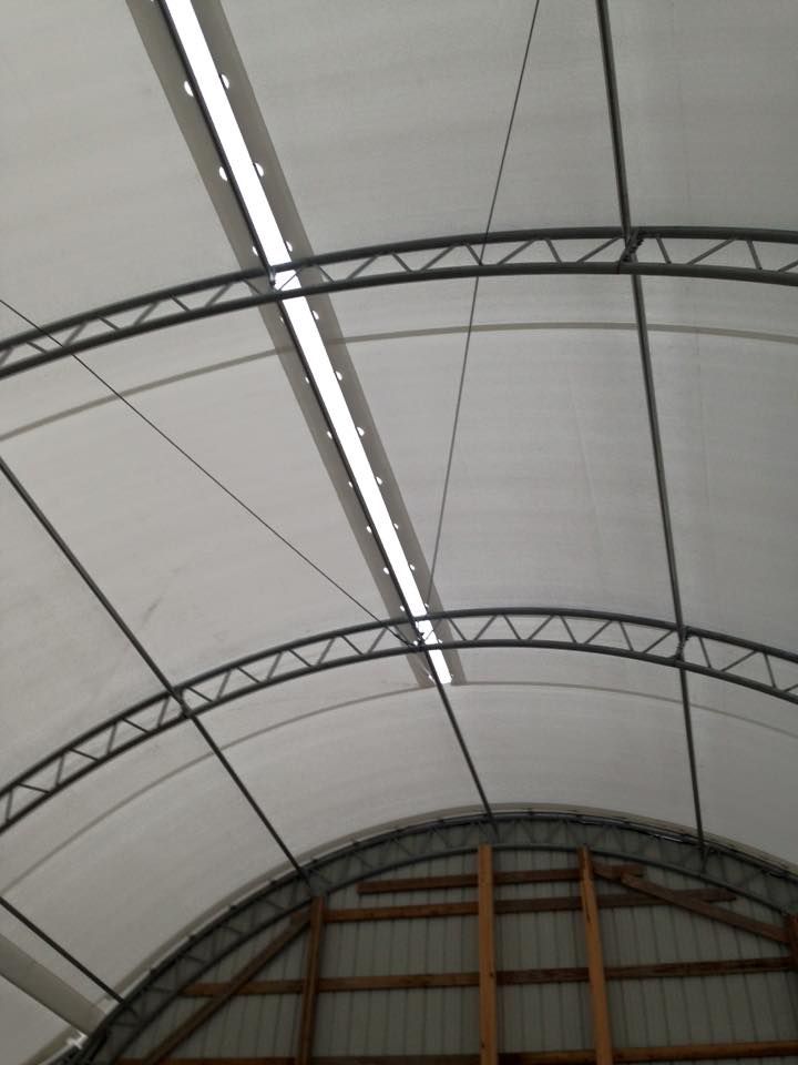 Interior view of a white fabric-covered arched roof with metal support beams and a central light fixture.