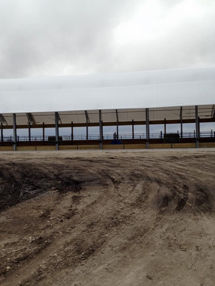 A long, covered structure with windows sits on a dirt lot under a cloudy sky.