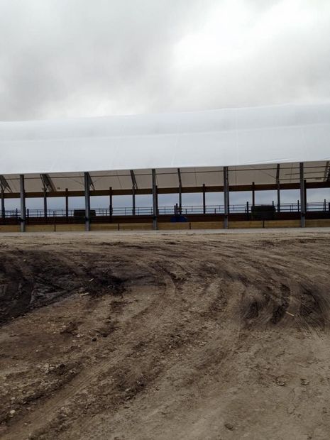 A long, covered structure with windows sits on a dirt lot under a cloudy sky.
