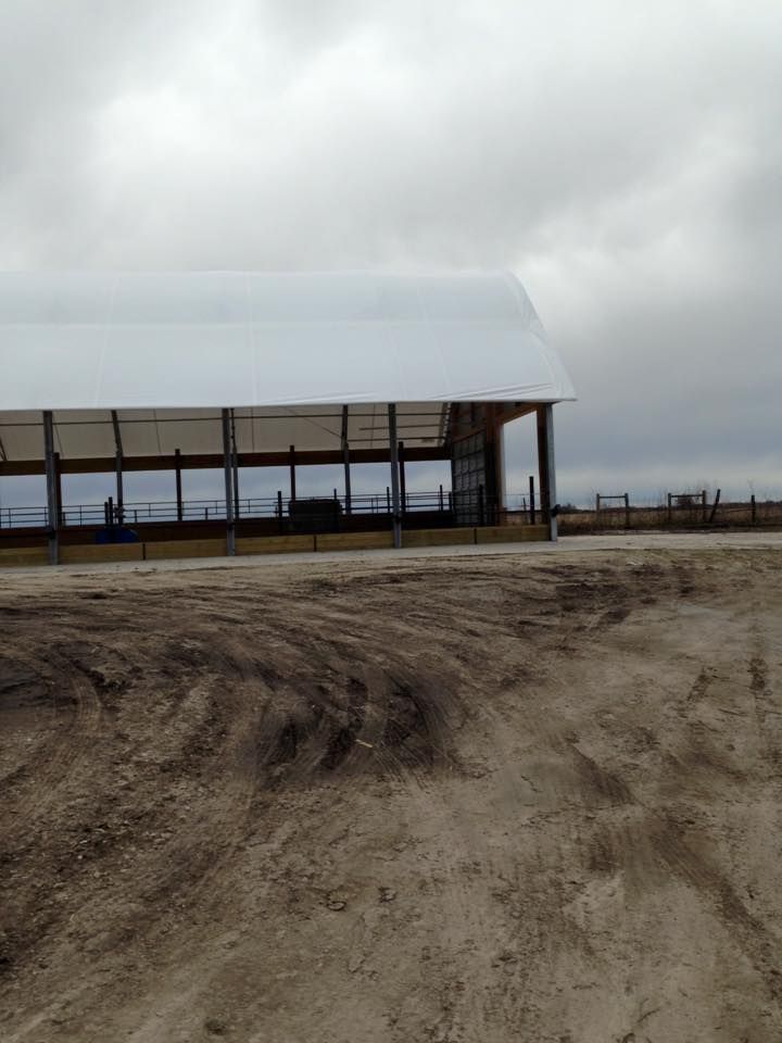 A large barn with a white roof on a cloudy day. Dirt road in the foreground.