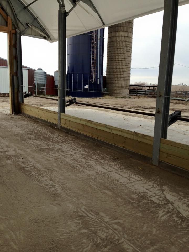 Concrete walkway with wooden barrier under a white awning, adjacent to a silo and a blue tank.