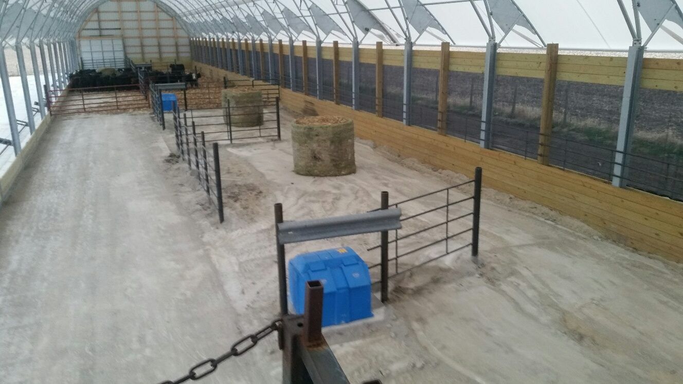 Inside a large barn-like structure with hay bales and fences, possibly for livestock.