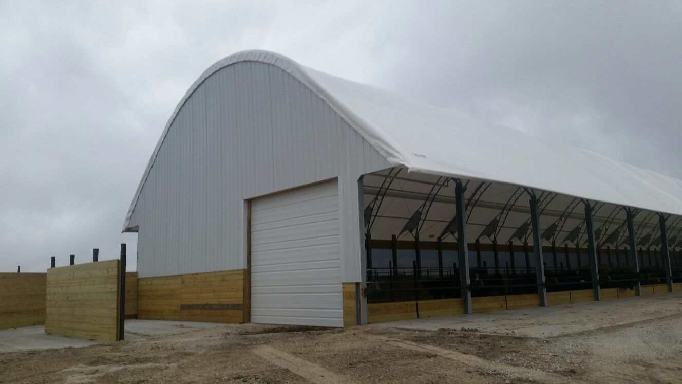 White arched-roof building with a large garage door, wood siding, and windows under a cloudy sky.