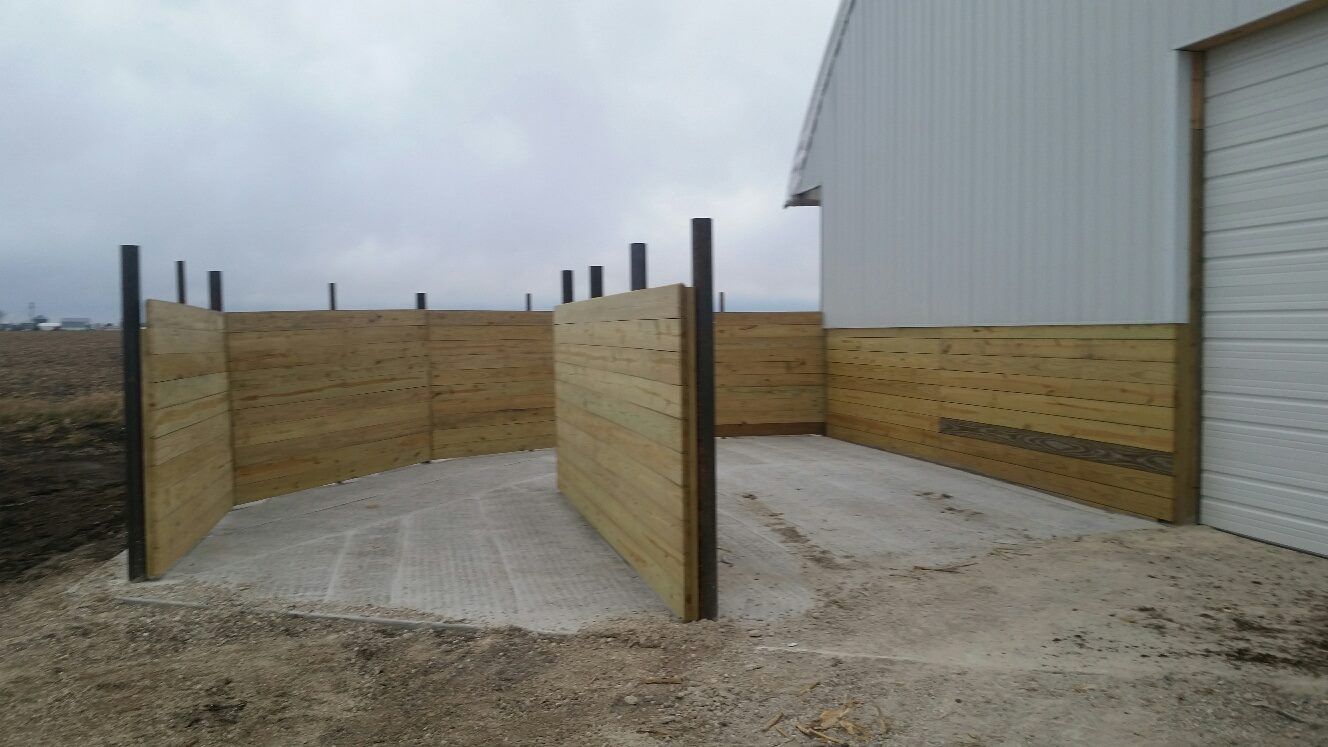 Wood and metal fence structure attached to the side of a white building with a concrete floor.