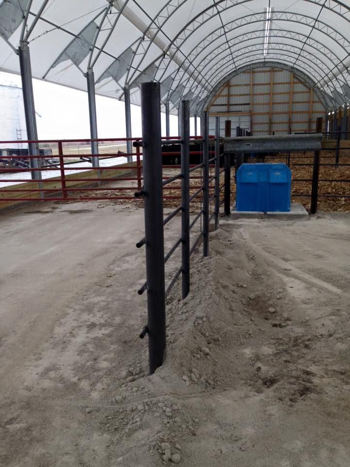 Black metal fence inside a large, white-roofed building. Sand ground. Blue box. Red fence in background.