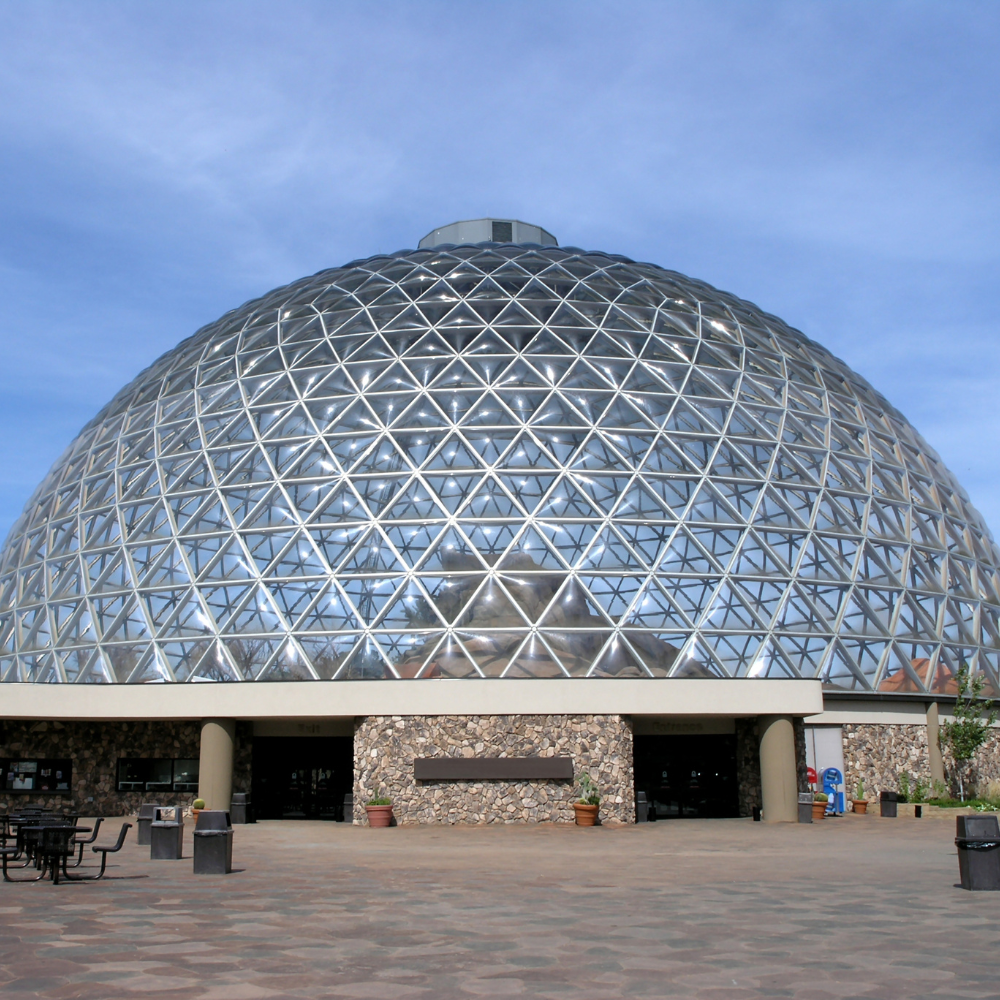 Large glass dome structure, brown stone base, blue sky background.