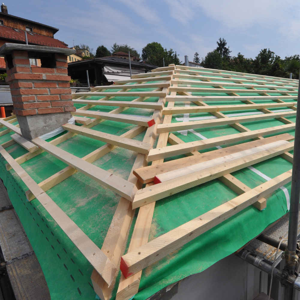 Roof under construction, wooden rafters over green waterproof membrane, with brick chimney.
