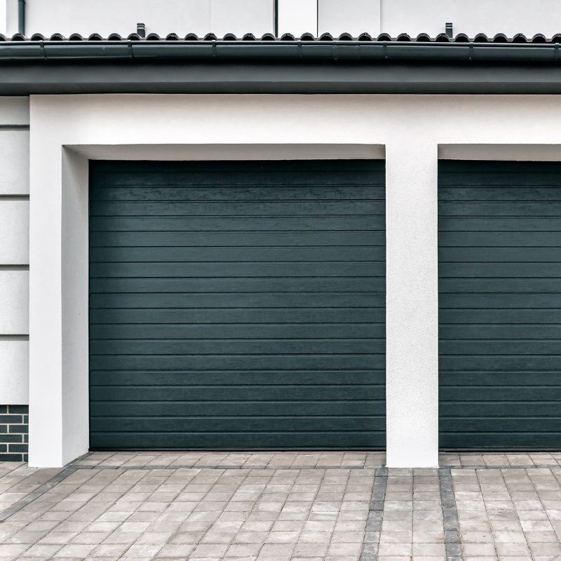 Two dark teal garage doors in a white frame, on a brick driveway.