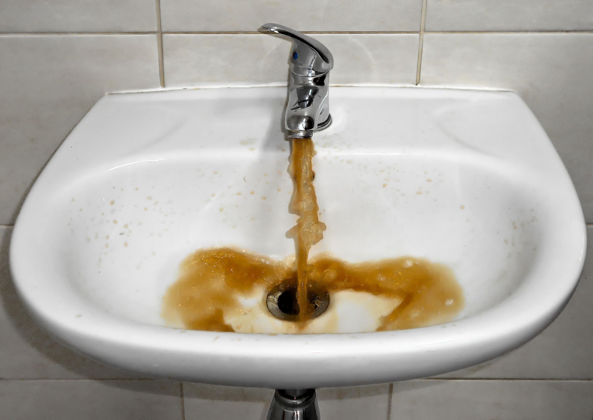 Brown water is coming out of a faucet in a bathroom sink