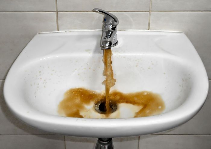 Brown water is coming out of a faucet in a bathroom sink