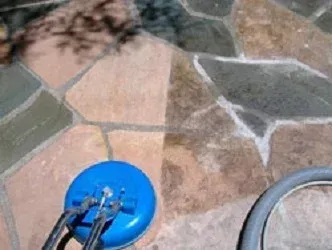 Blue pressure washer cleaning a multicolored stone patio.