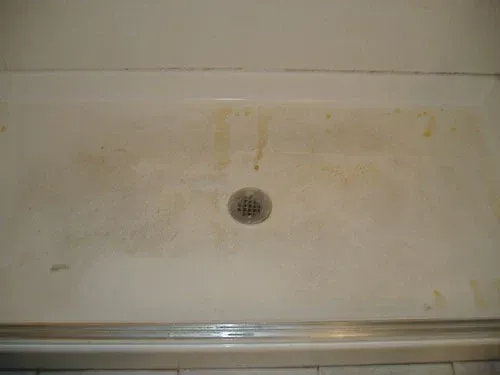 Dirty, stained white shower pan with drain.