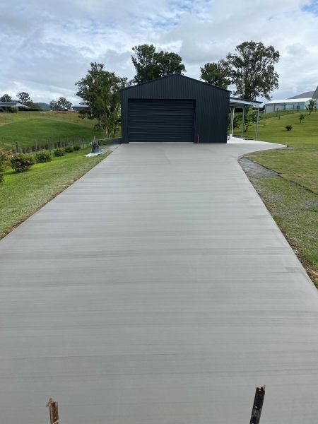 A Concrete Driveway Leading to a Garage With a Black Garage Door — Peter Bishop Concreting In Mary Valley, QLD