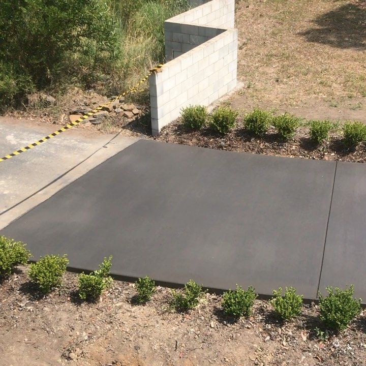 A Black Concrete Driveway With a Brick Wall in the Background — Peter Bishop Concreting In Widgee, QLD