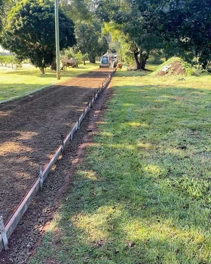 A Dirt Road Going Through a Grassy Field With Trees in the Background — Peter Bishop Concreting In Pomona, QLD