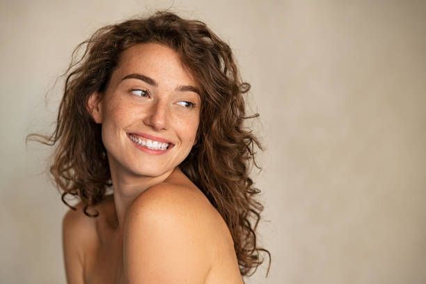 Smiling woman with glowing skin and curly hair after a facial skincare treatment at Tan Your Hide 