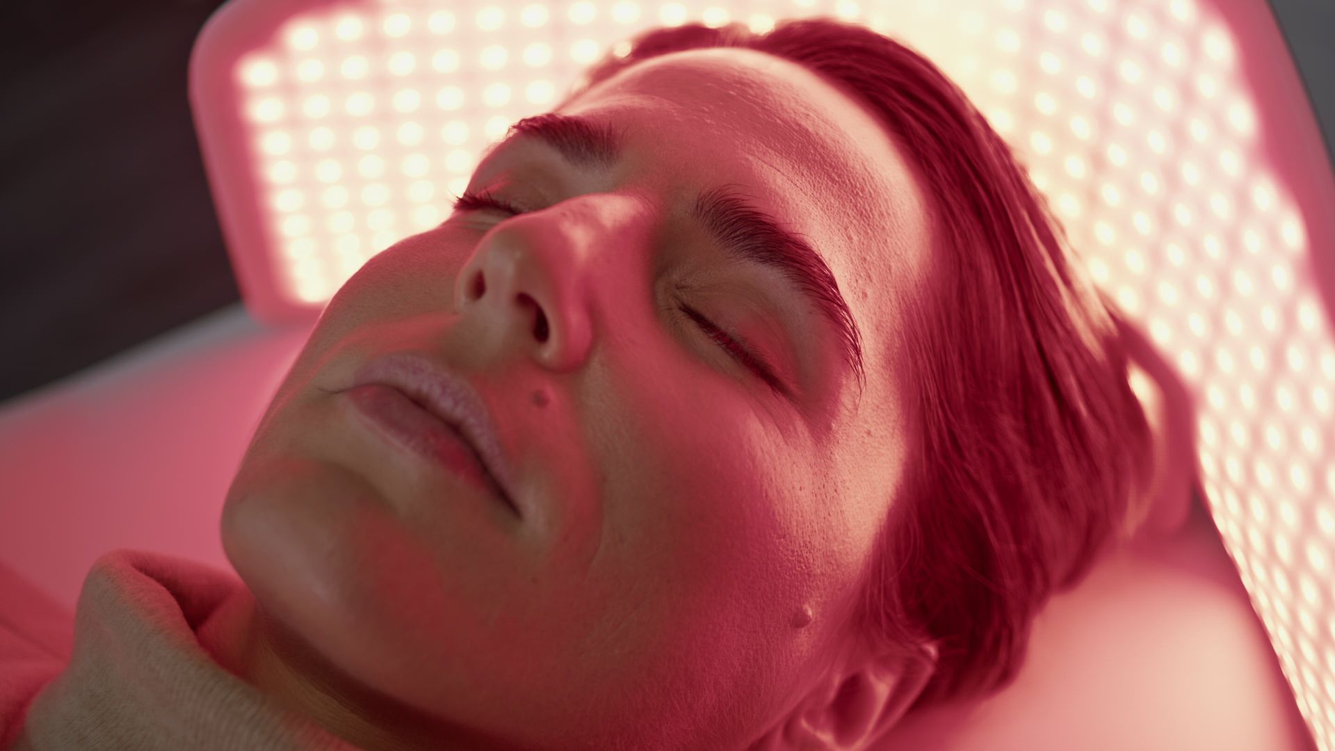 Person with closed eyes undergoing red light therapy.