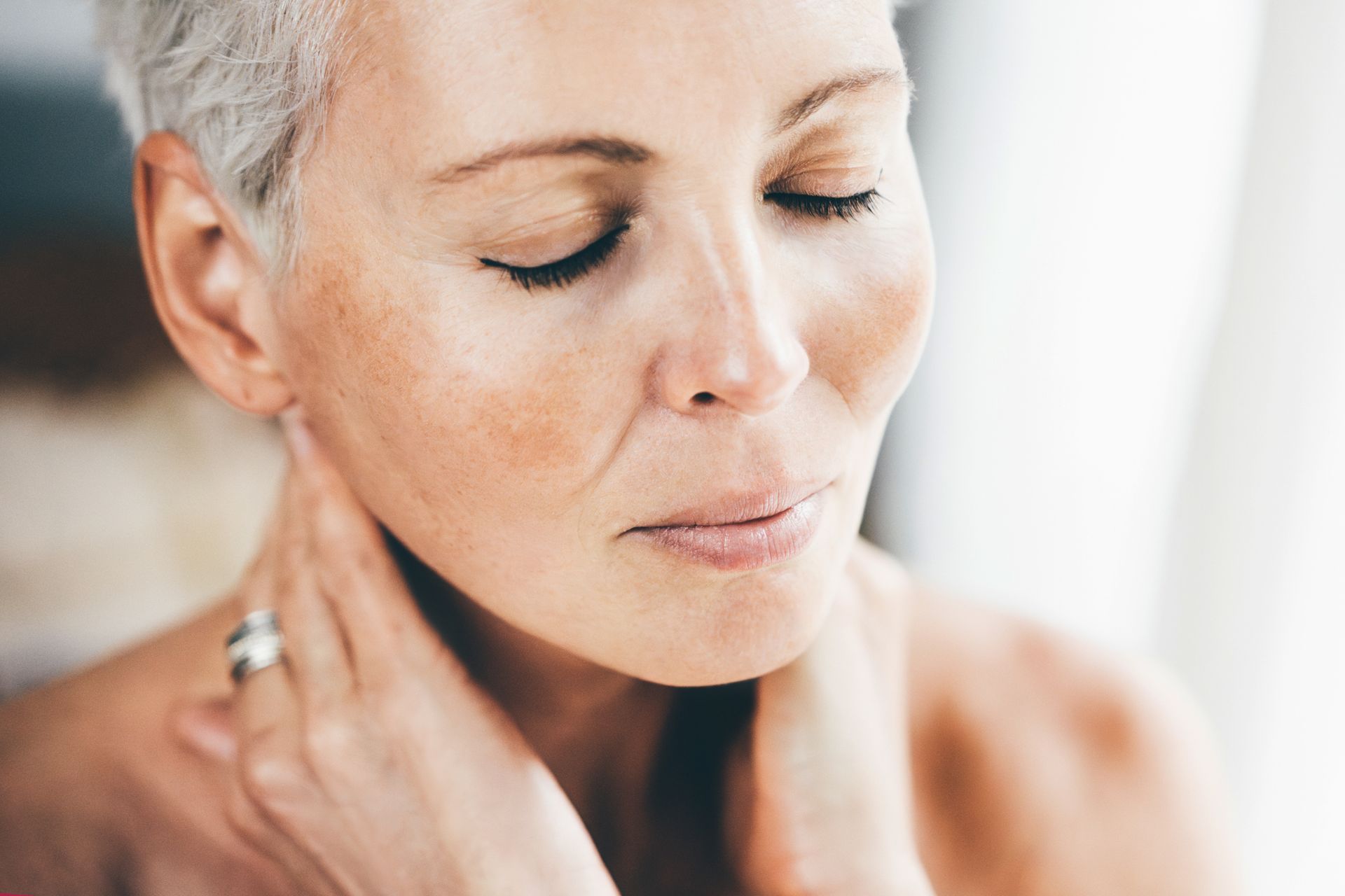 Closeup to an elderly woman touching the skin of her face and neck.
