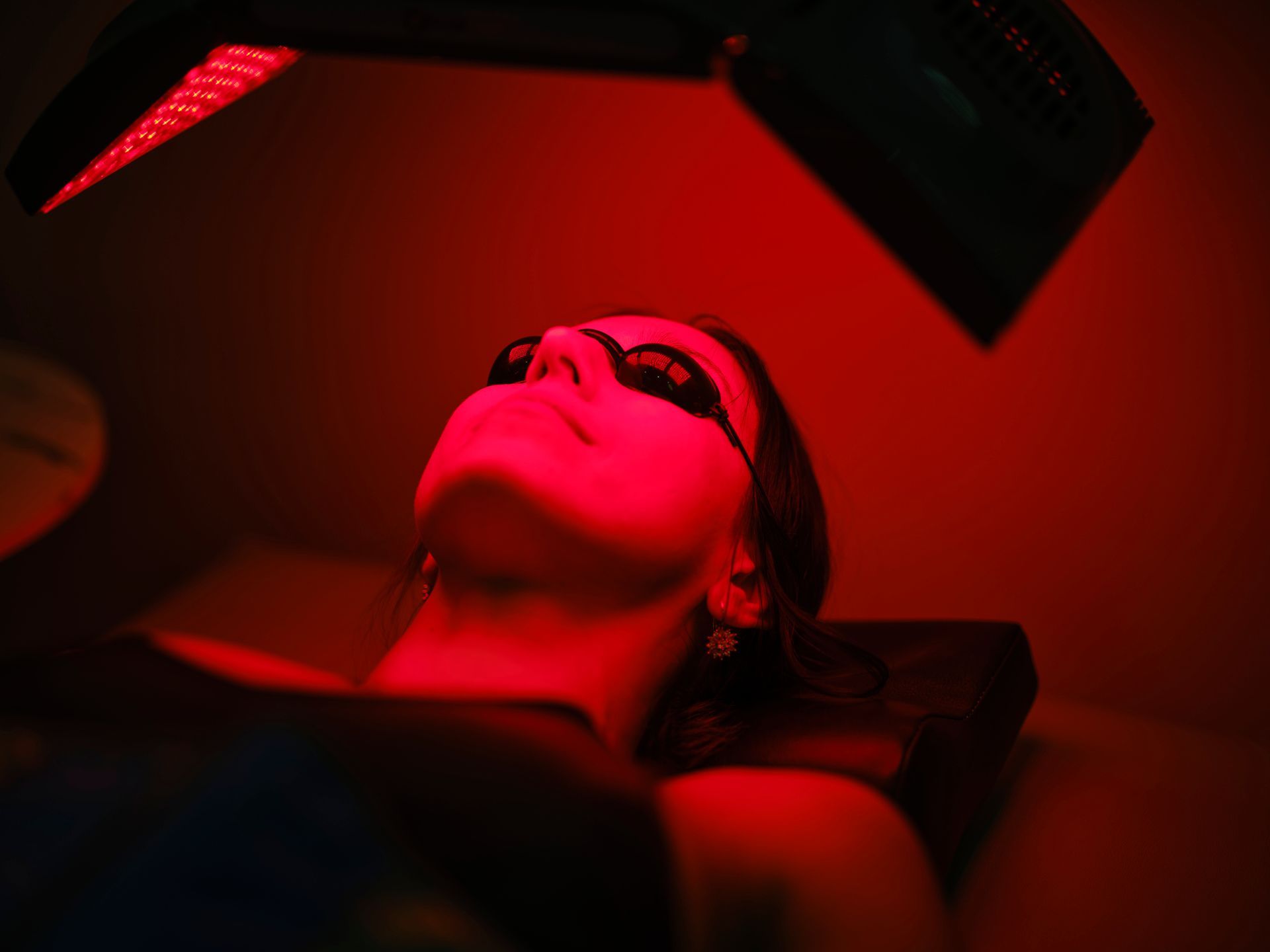 A woman is receiving red light therapy on an LED bed at a spa for skin rejuvenation.