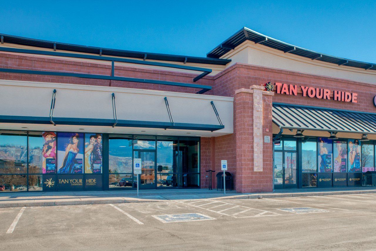 A tan your hide store with a parking lot in front of it.