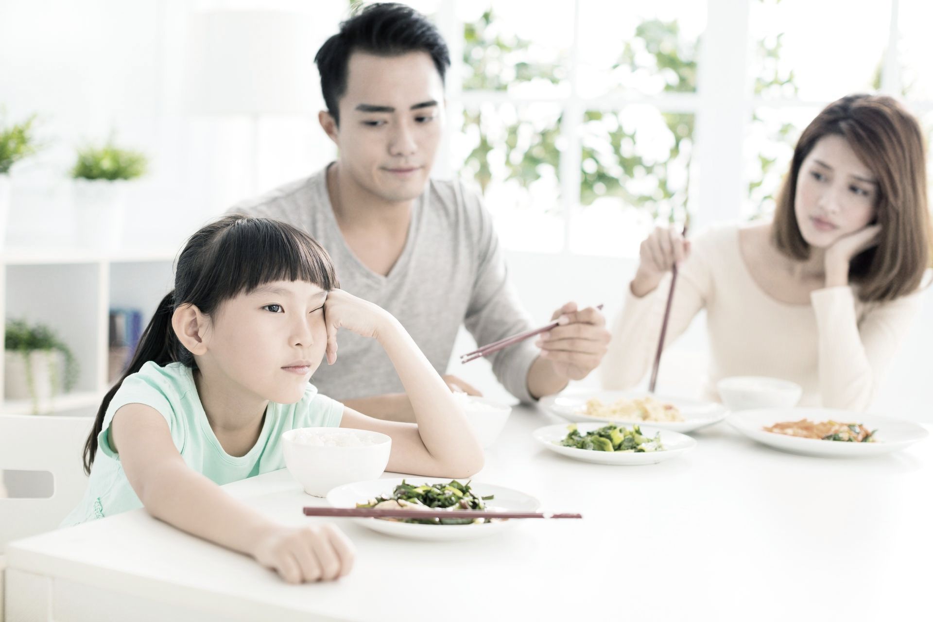 A girl sat at the table looking uninterested, and man and woman sat next to her with a negative look