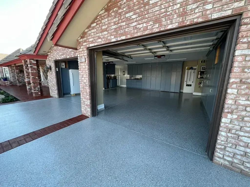 Open garage with speckled gray floor and brick exterior, leading into a clean empty interior.