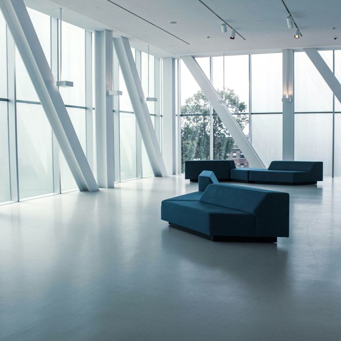 Modern minimalist lounge with blue sofas, white floors, and tall glass windows by angled pillars