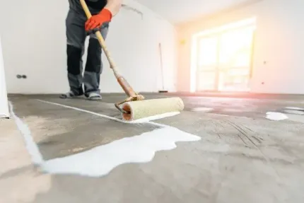 Person rolling white paint on a concrete floor in a bright room