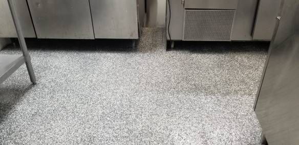 Stainless steel kitchen equipment on a speckled gray floor in a commercial kitchen.